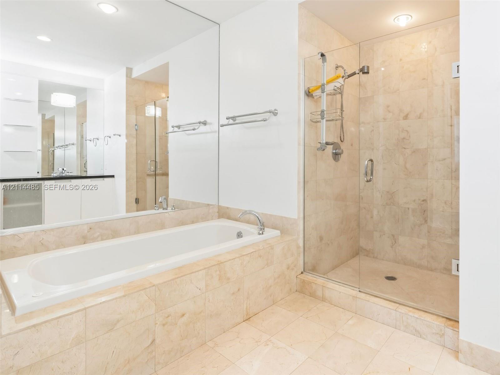 Bathroom featuring a tiled soaking tub, separate glass-enclosed shower, expansive wall-to-wall mirror, built-in cabinetry with a countertop, and recessed lighting