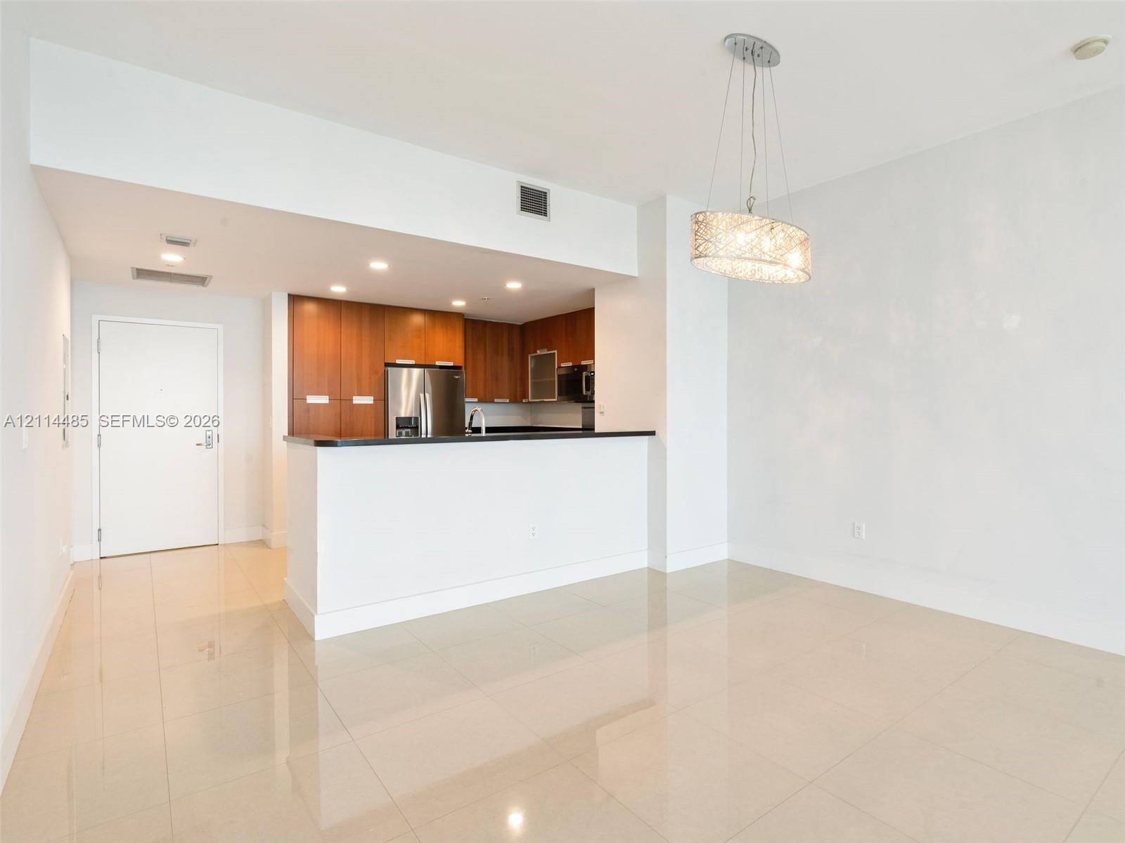 Kitchen featuring wood-finish cabinetry, a breakfast bar with stone-surface countertop, stainless steel appliances, polished tile flooring, and a decorative pendant light fixture