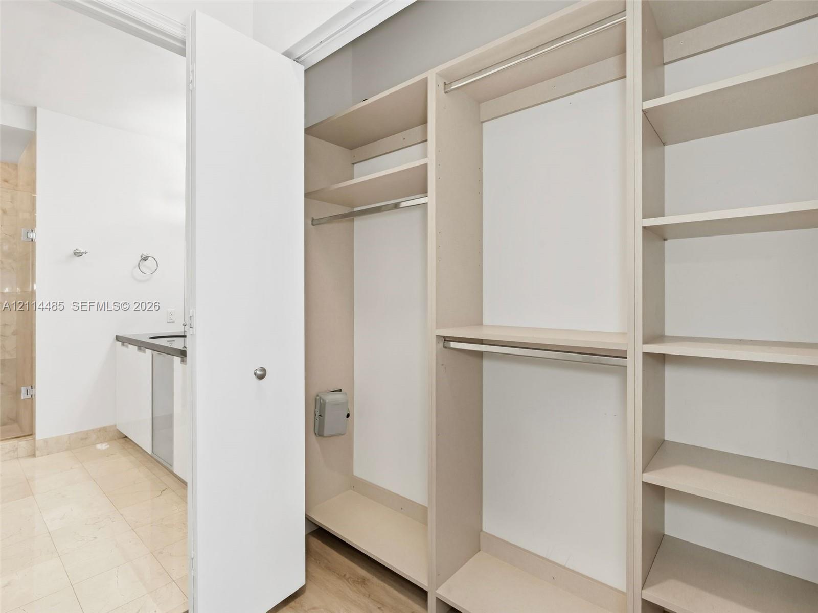 Custom walk-in closet featuring built-in shelving and dual metal hanging rods, paired with a bathroom containing a stone-surfaced vanity and tiled flooring