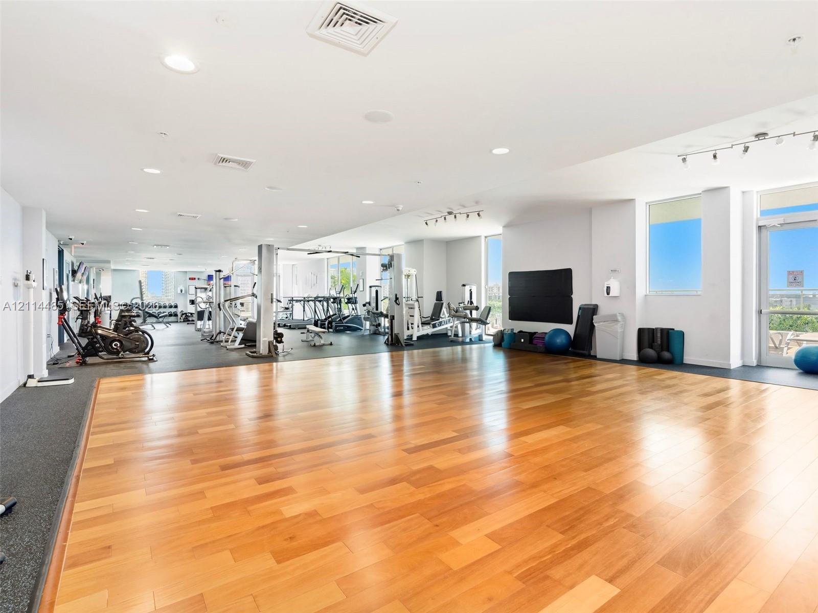 Fitness center featuring wood-finish flooring, rubberized exercise zones, recessed lighting, and expansive floor-to-ceiling windows