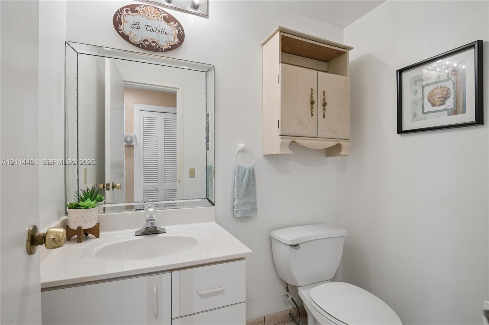 Bathroom featuring a white vanity cabinet with a stone-finish countertop, an oval undermount sink, a beveled-edge wall mirror, and a wall-mounted wooden storage cabinet