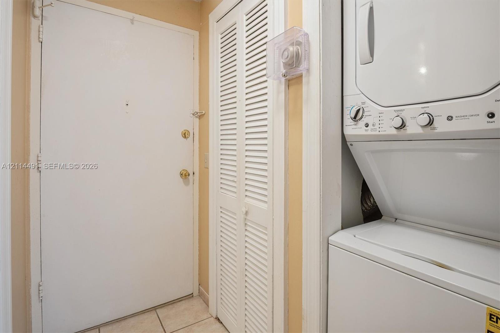 Laundry area featuring a stackable washer and dryer unit, louvered closet doors, and tile flooring