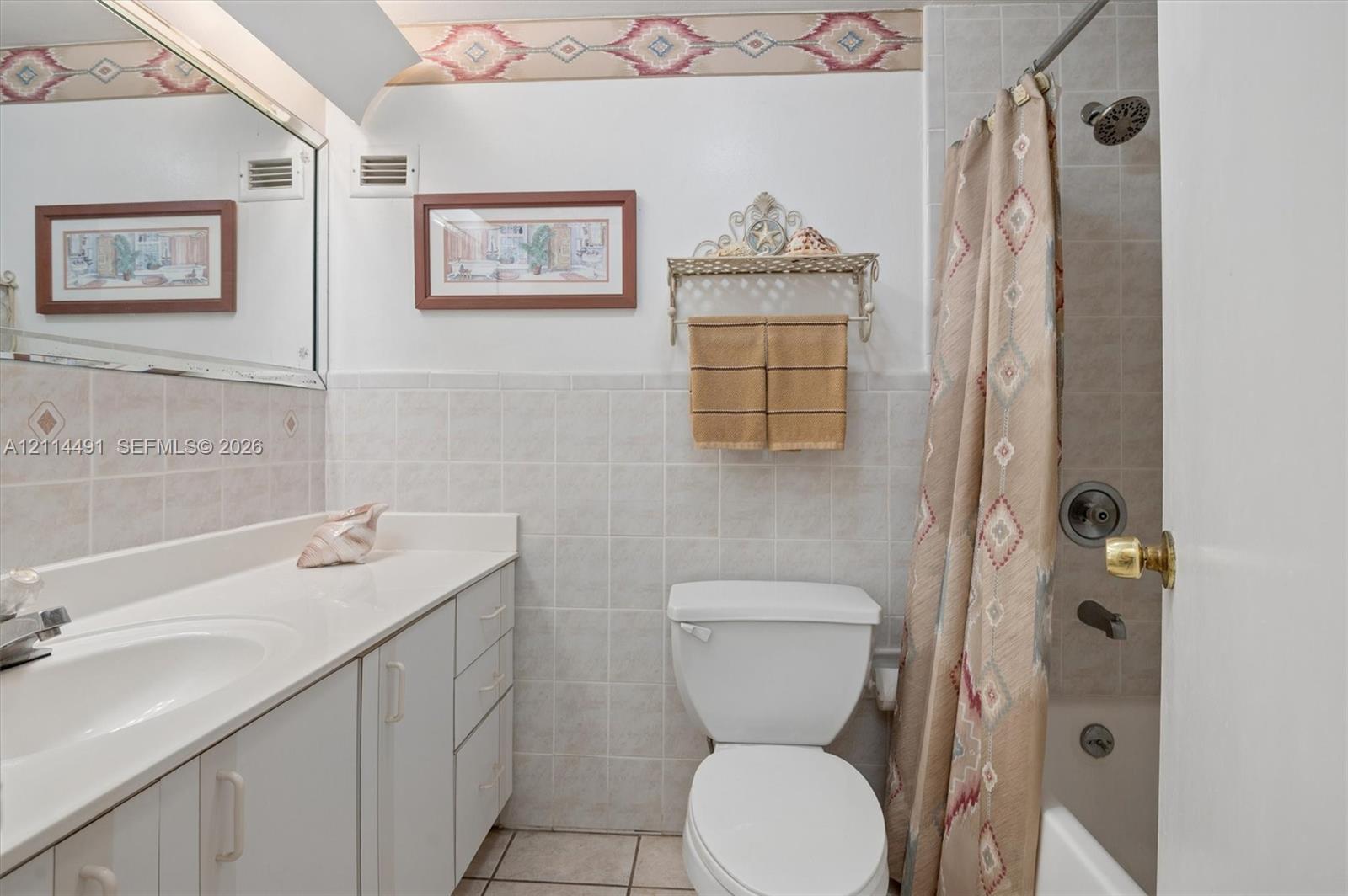 Bathroom featuring a white vanity with an integrated basin, wall-to-wall mirror, ceramic tile wainscoting, and a shower-tub combination with chrome fixtures