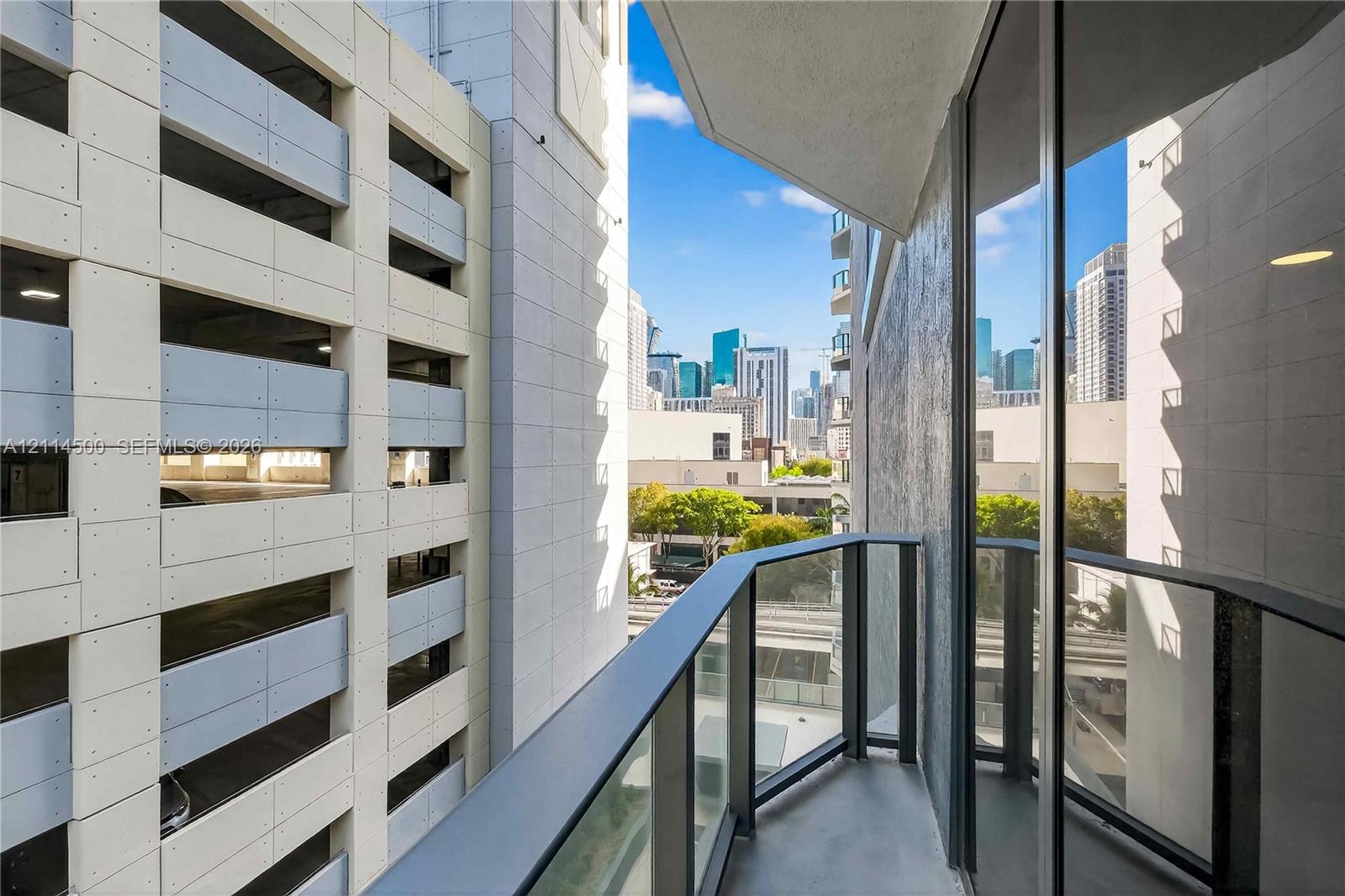 Covered balcony with black metal railings and glass panels, featuring urban skyline surroundings