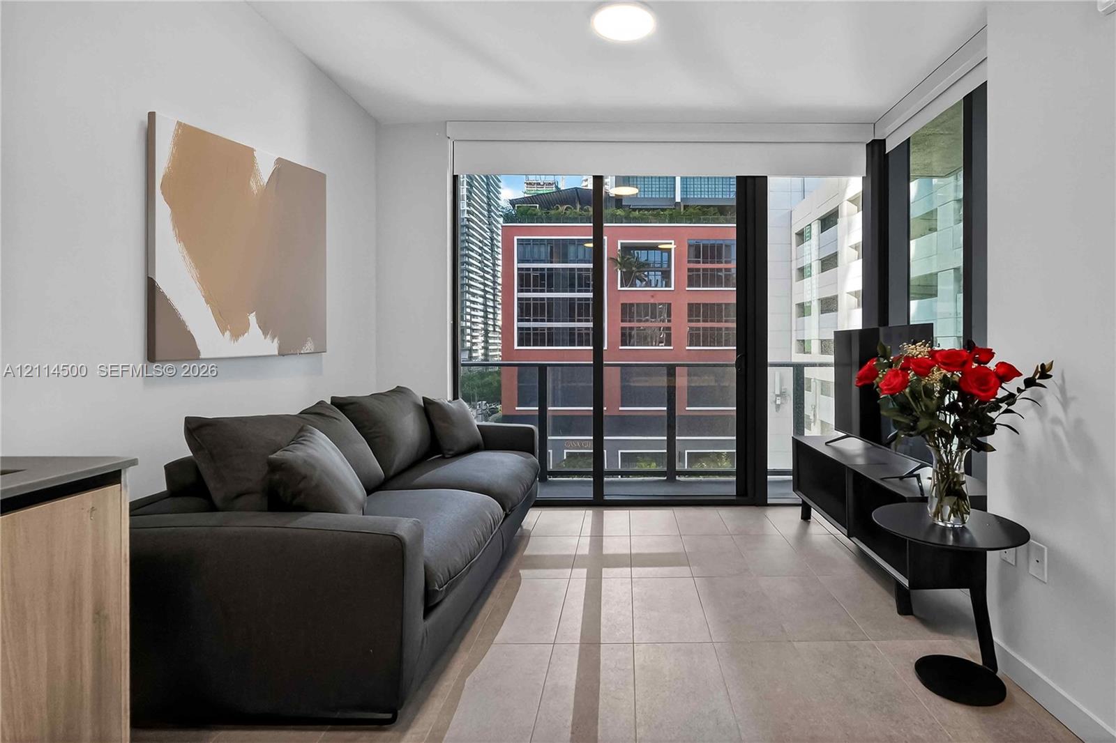 Floor-to-ceiling sliding glass doors, neutral tile flooring, and a private balcony with black metal railings
