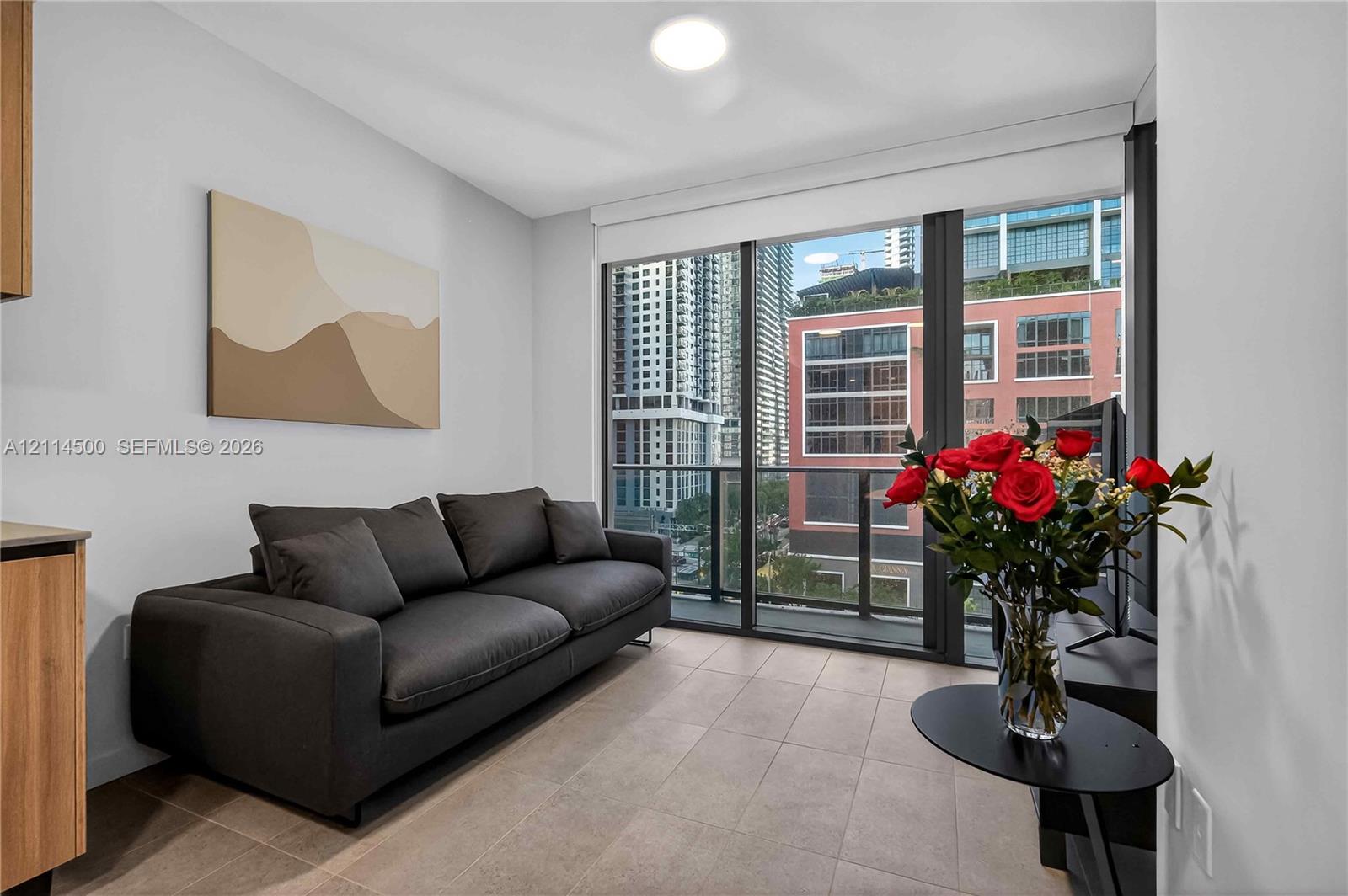 Floor-to-ceiling glass windows, neutral tile flooring, and integrated balcony access featuring metal railings
