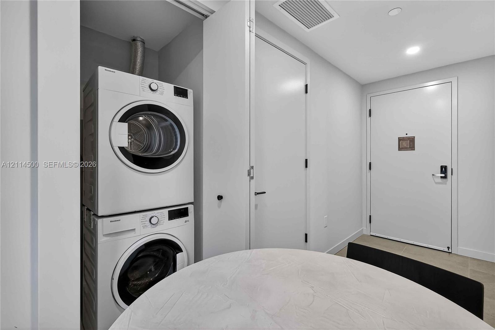 Utility area featuring stacked white laundry appliances, recessed lighting, and a white interior door with metallic hardware