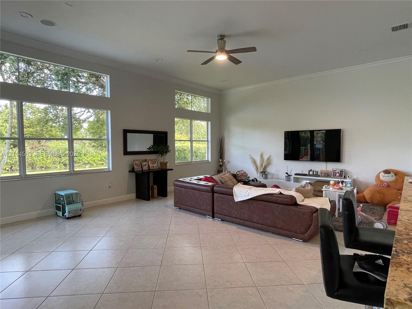 Living area featuring high ceilings, large windows with transom panels, ceramic tile flooring, and a ceiling fan