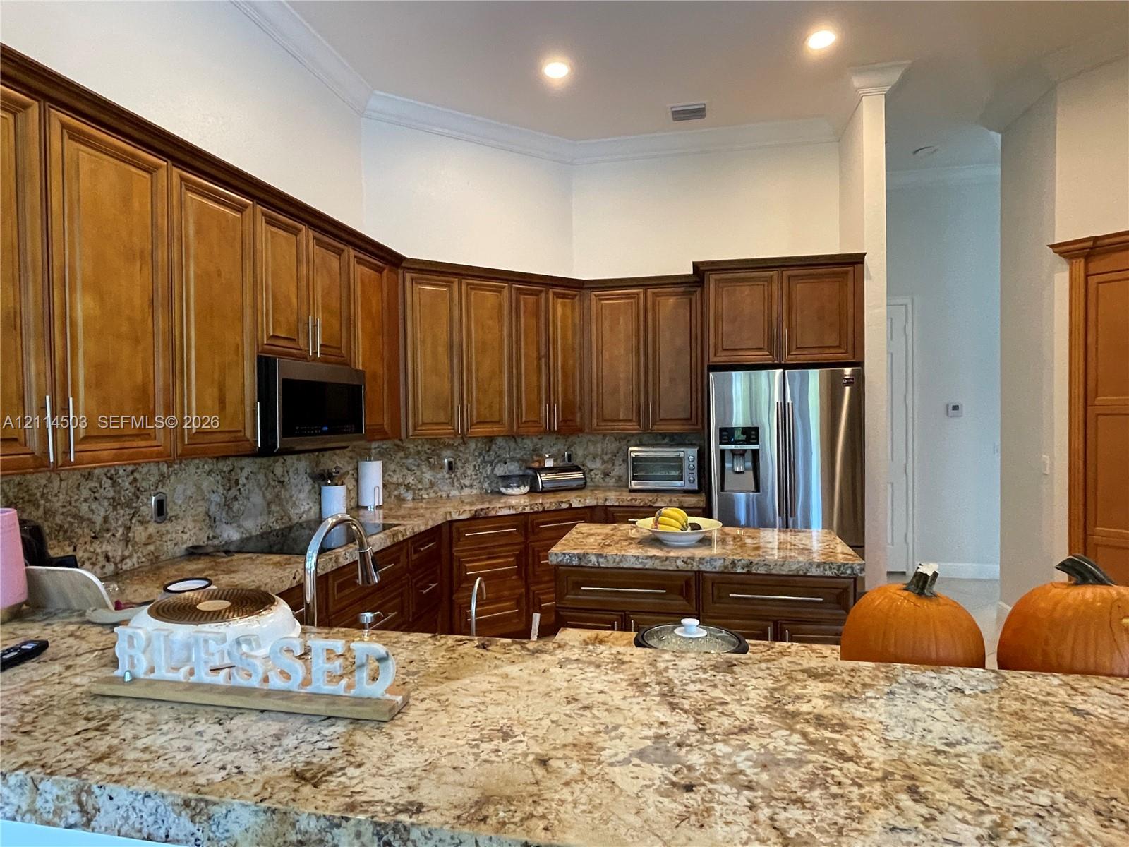 Kitchen featuring warm-tone wood cabinetry, stone countertops, stainless steel appliances, a central island, and crown molding
