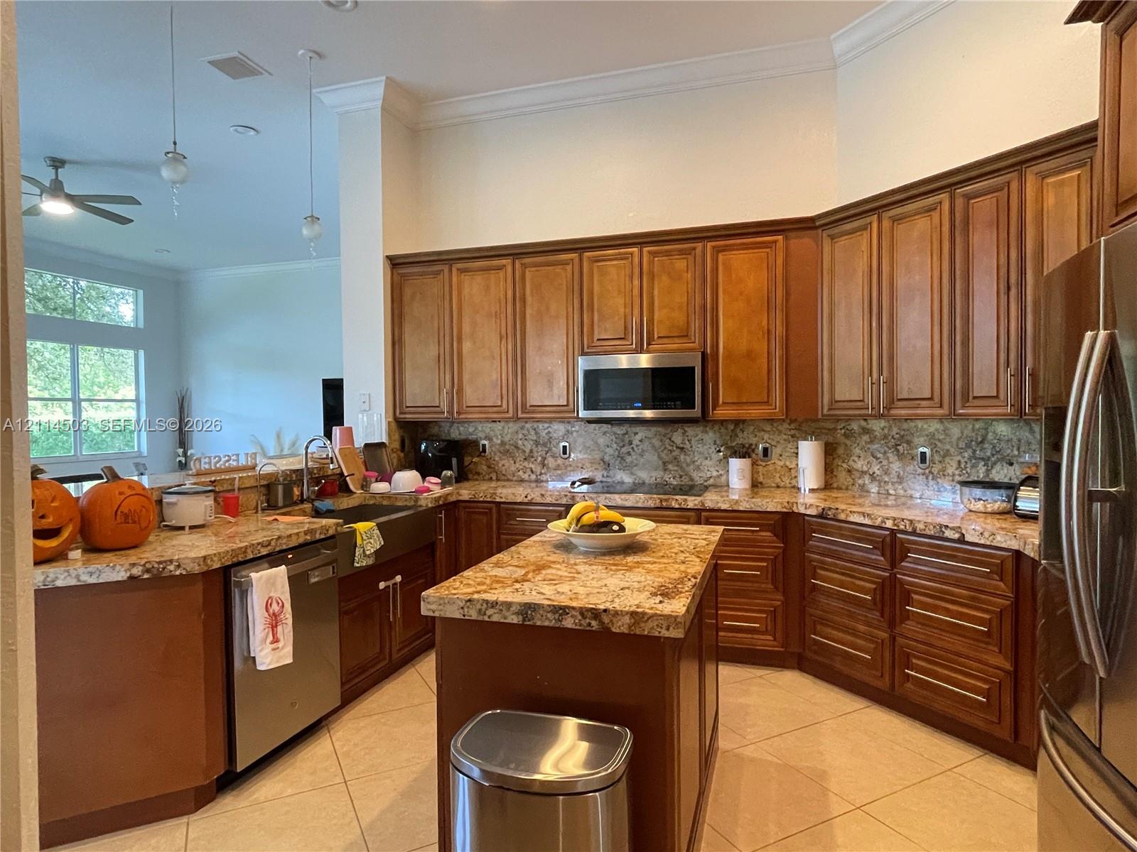 Kitchen featuring stained wood cabinetry, stone countertops, central island, stainless steel appliances, and tile flooring