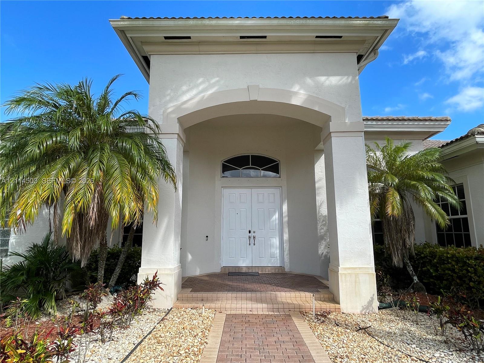 Stucco exterior featuring a covered entryway, double-door entrance with an arched transom window, and a brick-paver walkway