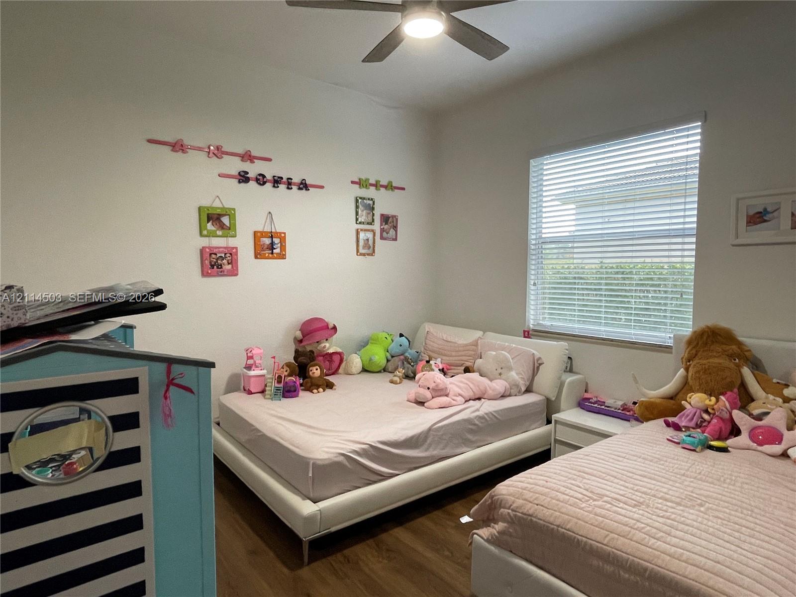 Bedroom featuring wood-finish flooring, a neutral color palette, a large window with horizontal blinds, and an integrated ceiling fan with light fixture