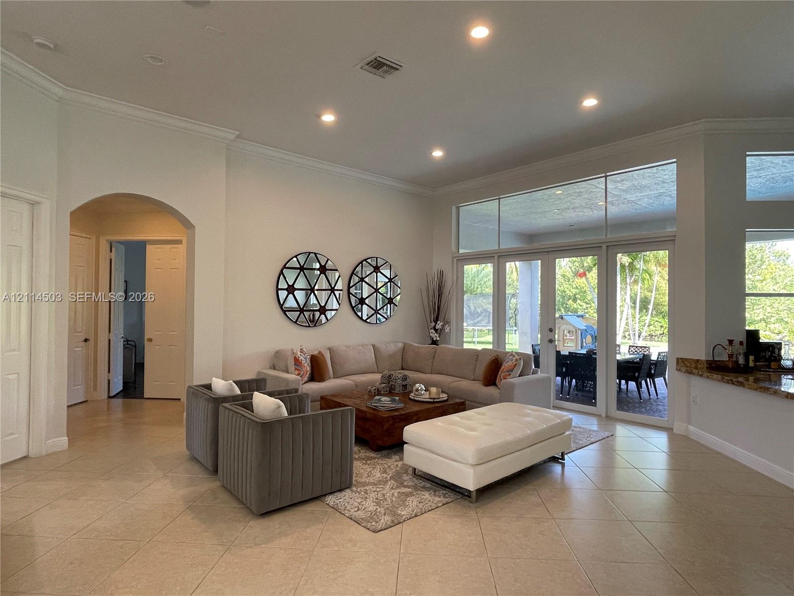 Open-concept living space featuring high ceilings with recessed lighting, large-format tile flooring, arched entryways, and floor-to-ceiling glass paneling with double doors