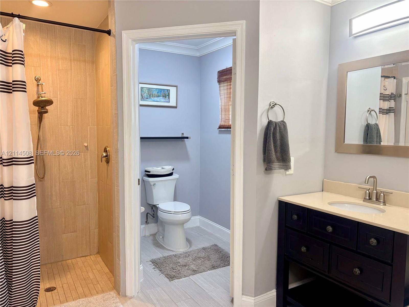 Bathroom featuring a dark wood-finish vanity with a light-toned countertop, shower enclosure with wood-finish tile surround, and a wall-mounted light fixture