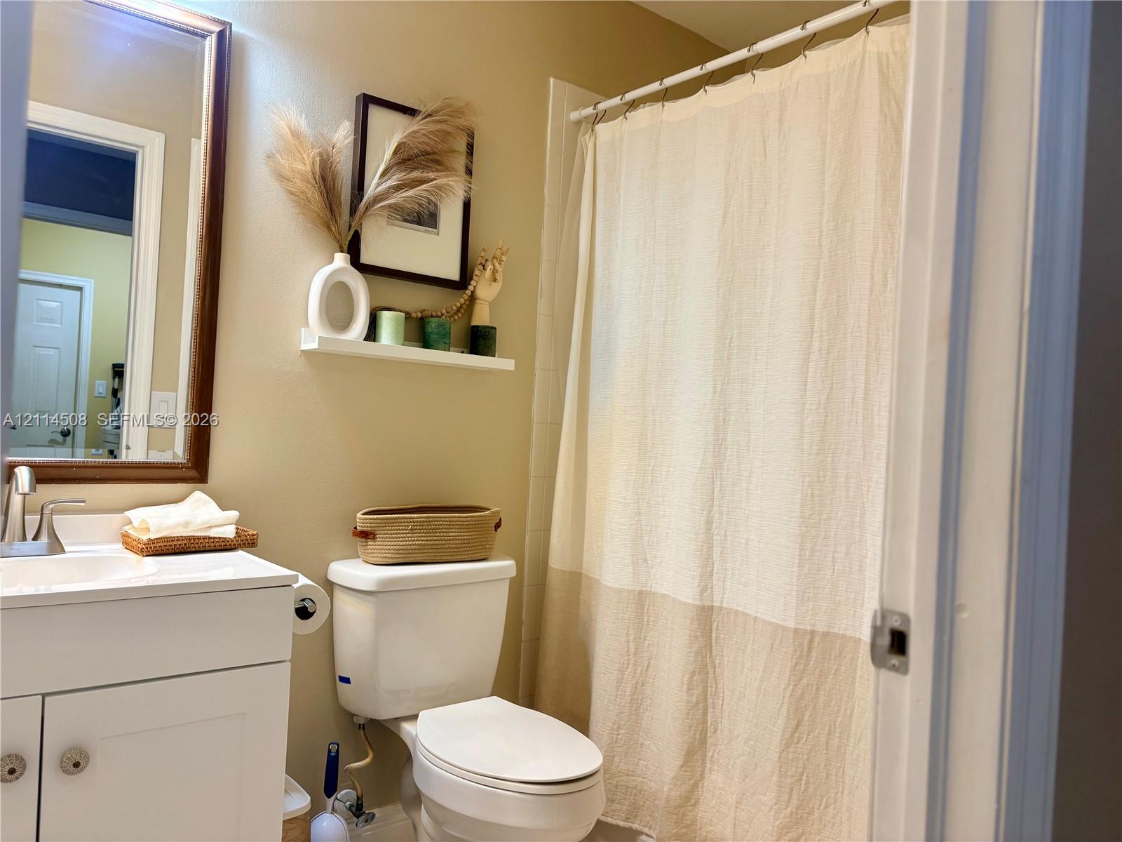 Bathroom featuring a white vanity with integrated basin, polished metal faucet, wood-framed mirror, built-in floating wall shelf, and shower-tub combination