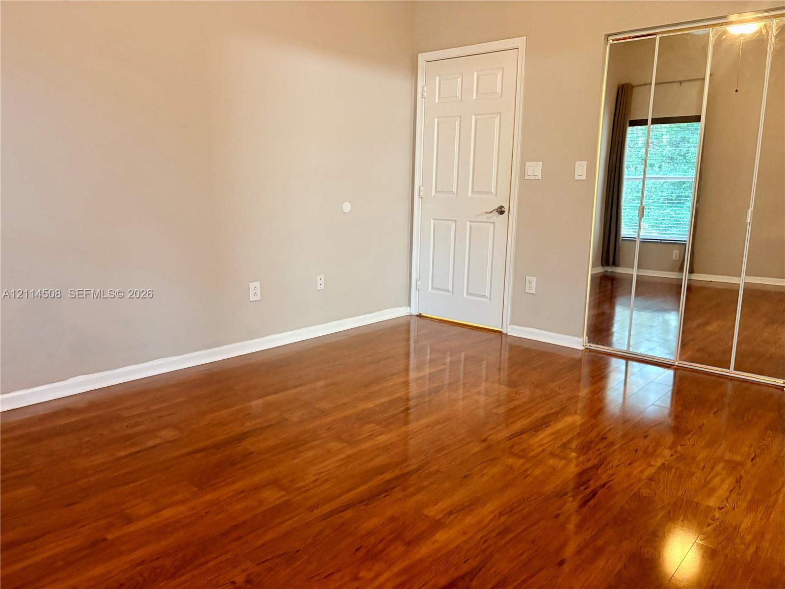 Room featuring wood-finish flooring, a neutral wall color palette, a classic six-panel interior door, and mirrored sliding closet doors