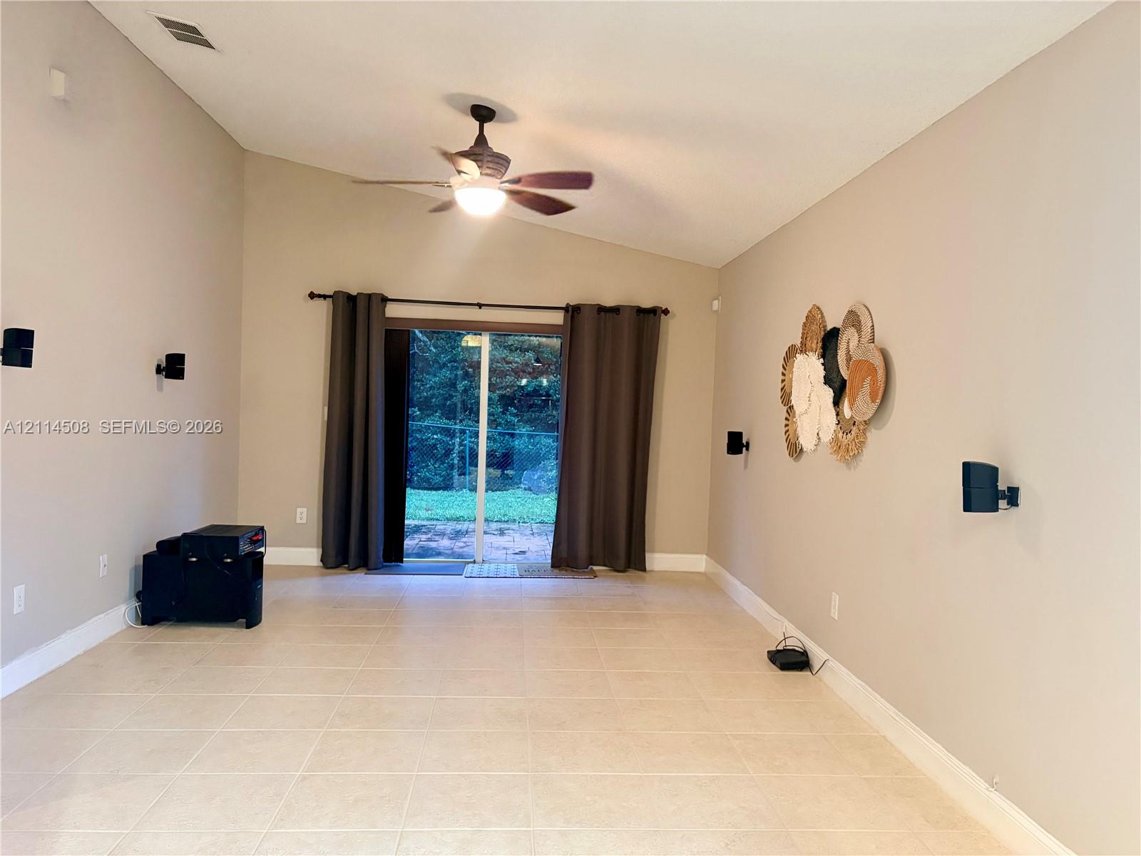 Vaulted ceilings, large-format tile flooring, and sliding glass doors leading to an exterior patio area, accented by a ceiling-mounted fan and wall-mounted audio speaker brackets
