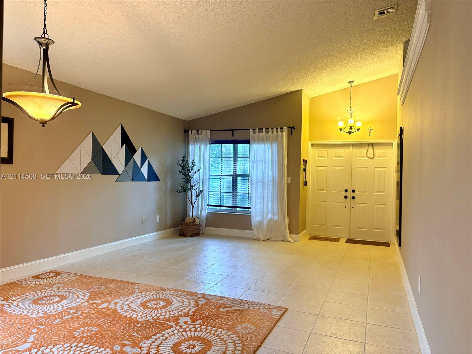 Vaulted ceilings featuring multi-tiered pendant lighting, tile flooring, and double-entry doors Vaulted ceilings featuring multi-tiered pendant lighting, tile flooring, and double-entry doors