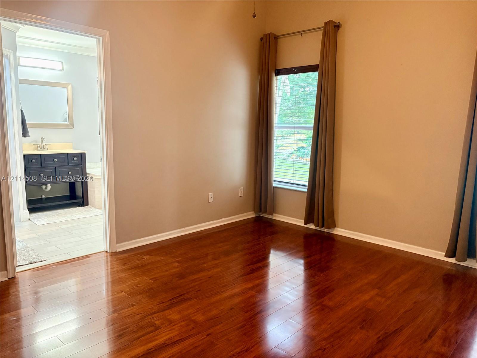 Room featuring wood-finish flooring, a single window, and a dark-toned vanity cabinet with a rectangular mirror and wall-mounted light fixture