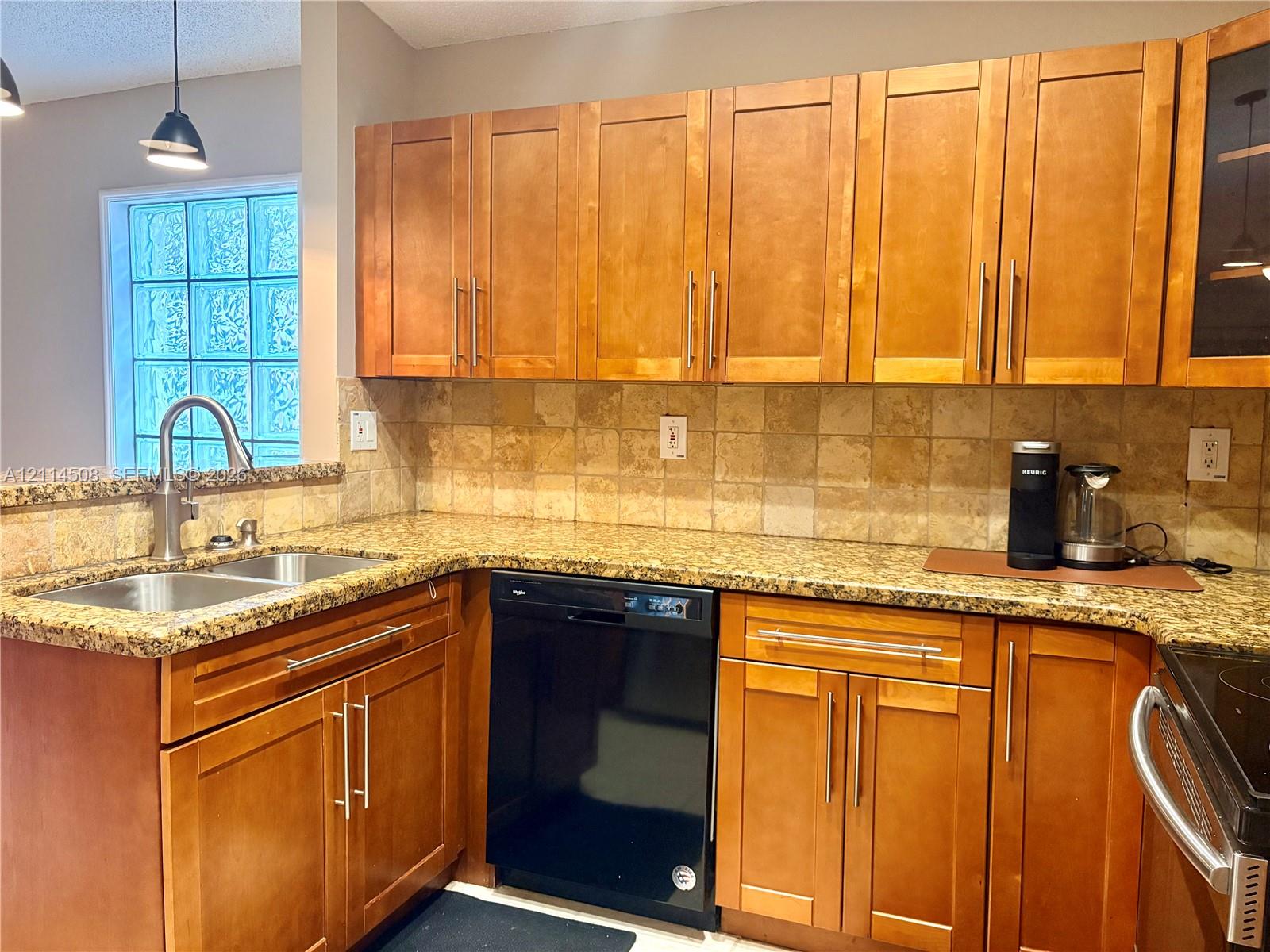 Kitchen featuring shaker-style wood cabinetry, stone countertops, square-tile backsplash, stainless steel dual-basin undermount sink with gooseneck faucet, and glass block window