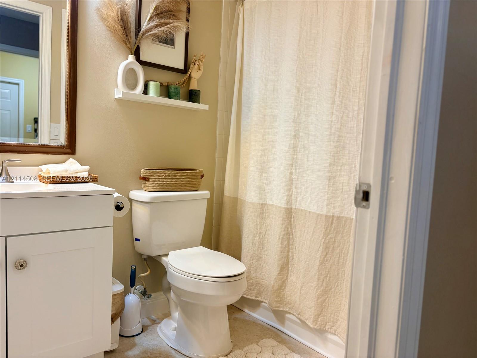 Bathroom featuring a white vanity cabinet, a wall-mounted shelf, a framed mirror with a wood-finish frame, and a tub-shower combination with a shower curtain