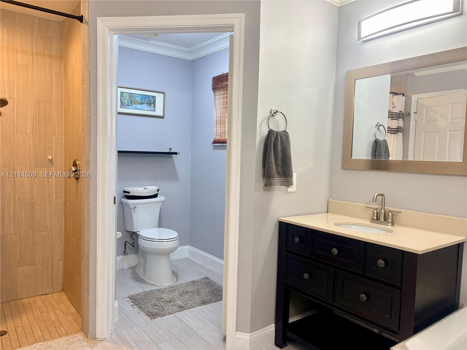 Bathroom featuring a dark-finish vanity with a light-toned countertop, a walk-in shower with vertical neutral tile, a built-in mirror, and a wall-mounted light fixture