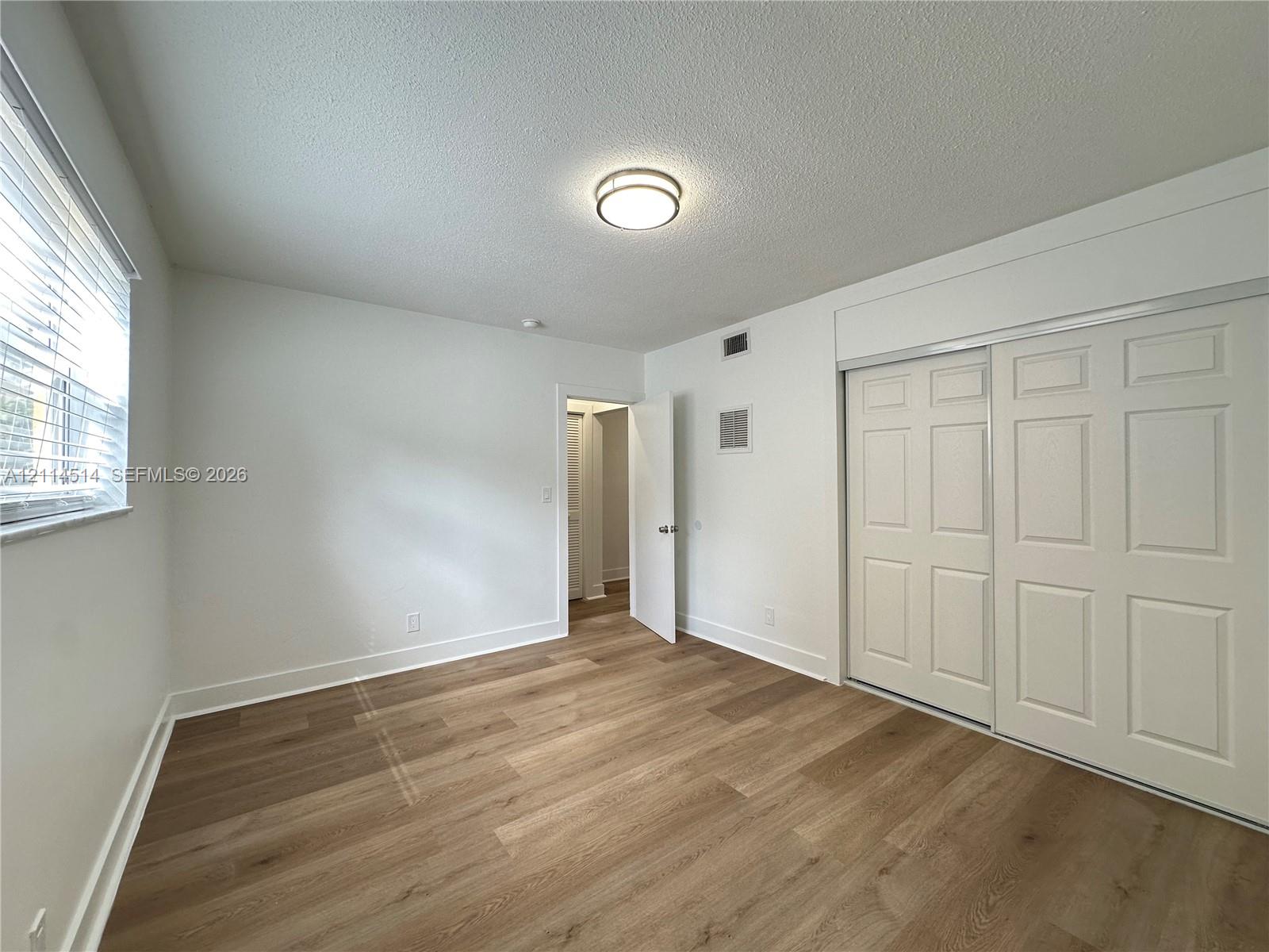 Room featuring wood-finish flooring, sliding closet doors with paneled detailing, neutral wall finishes, and a flush-mount circular lighting fixture