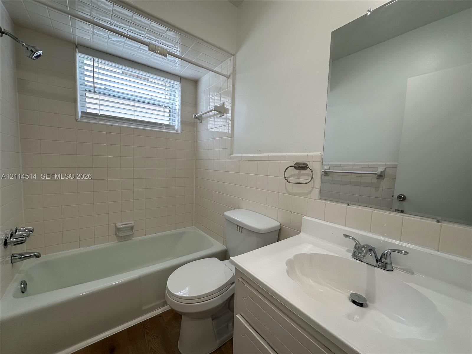 Bathroom featuring a vanity with a white integrated sink, chrome dual-handle faucet, wall-mounted mirror, and tile-surround shower and bathtub combination Bathroom featuring a vanity with a white integrated sink, chrome dual-handle faucet, wall-mounted mirror, and tile-surround shower and bathtub combination