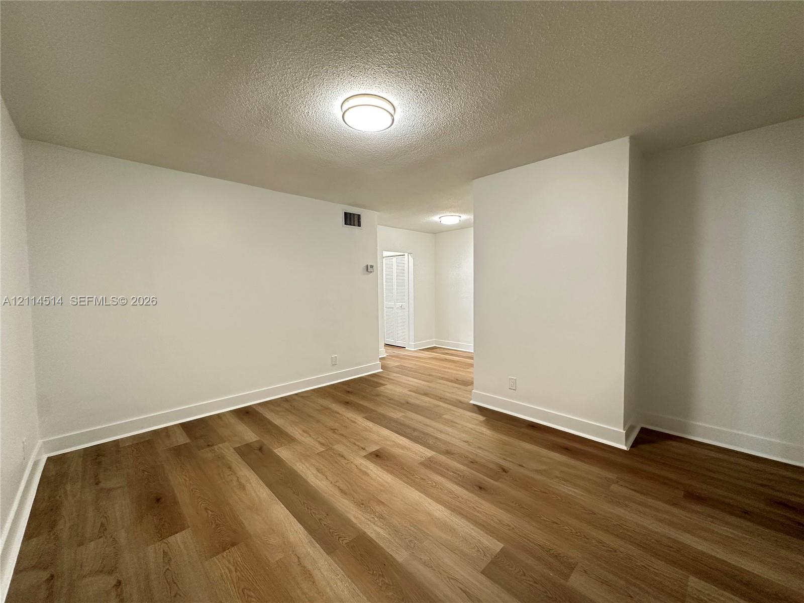 Interior space featuring wood-finish flooring, white walls, and flush-mount ceiling lighting Interior space featuring wood-finish flooring, white walls, and flush-mount ceiling lighting