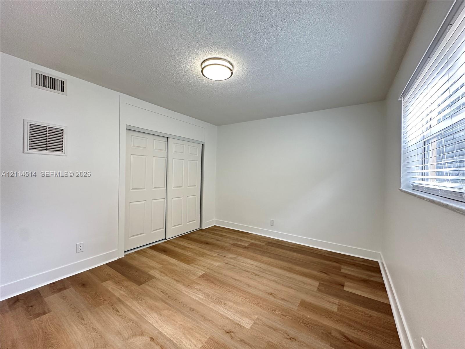 Neutral interior space featuring wood-finish flooring, sliding closet doors with raised panel detail, and a flush-mount circular ceiling fixture