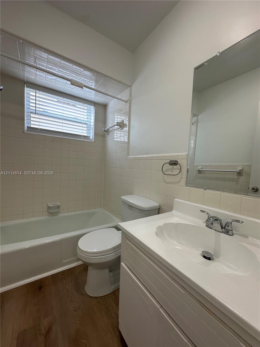 Bathroom featuring a white vanity with an integrated basin, wood-finish flooring, tiled shower surround, and a recessed mirror Bathroom featuring a white vanity with an integrated basin, wood-finish flooring, tiled shower surround, and a recessed mirror