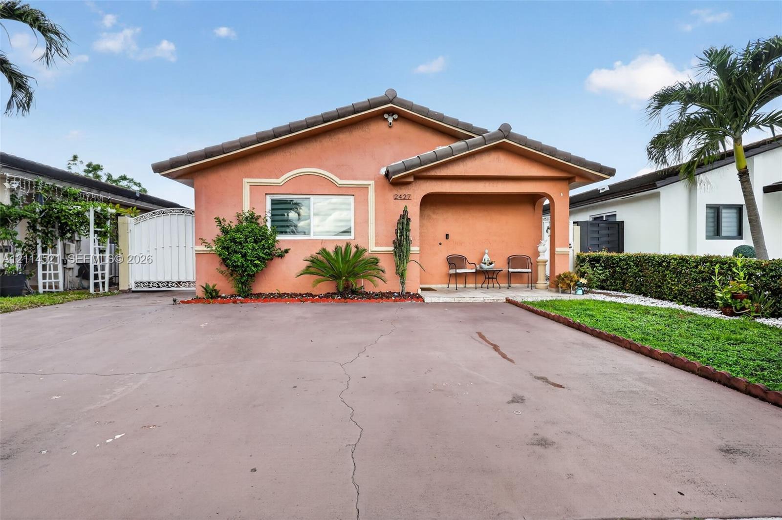 Stucco exterior featuring a covered front porch, hip roofline, decorative window molding, and expansive paved driveway