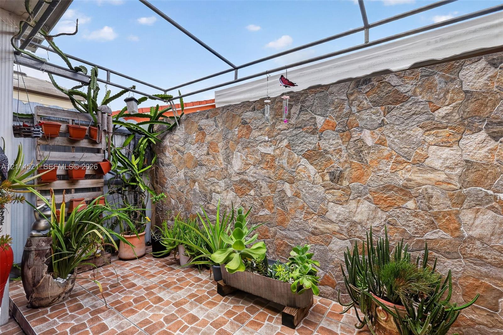 Outdoor patio featuring natural stone wall cladding, tiled flooring, and a metal frame overhead structure