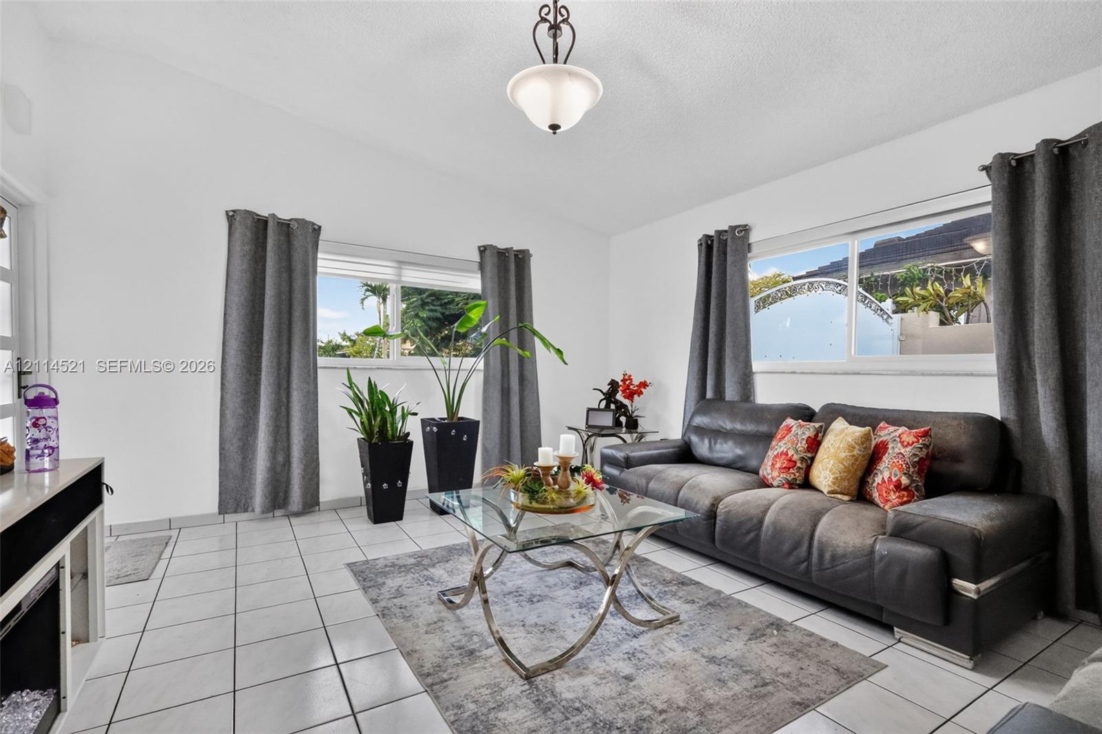 Living area featuring light-toned ceramic tile flooring, vaulted ceilings, dual-pane windows, and a central pendant light fixture Living area featuring light-toned ceramic tile flooring, vaulted ceilings, dual-pane windows, and a central pendant light fixture