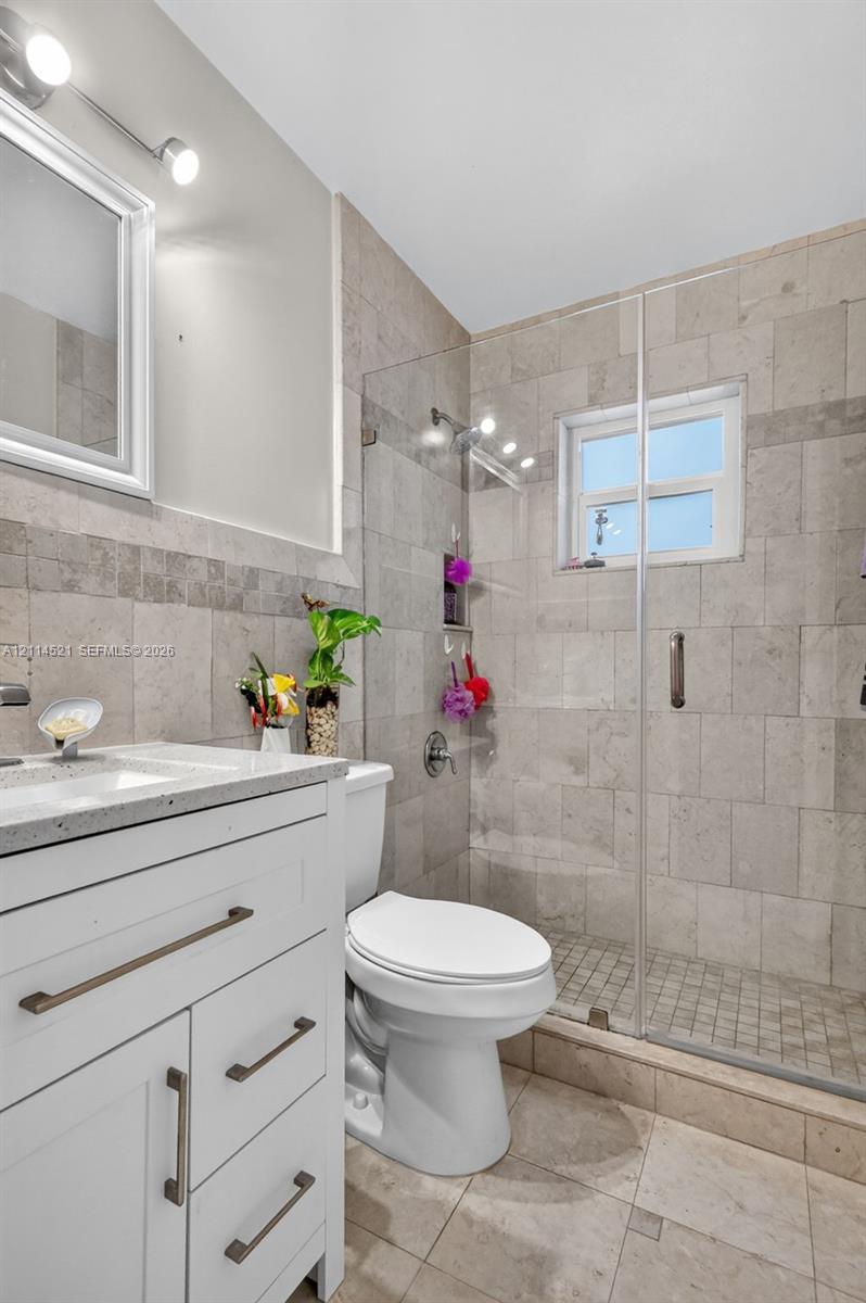 White shaker-style vanity with stone-finish countertop, frameless glass shower enclosure, full-height wall tiling, and dual-light vanity fixture