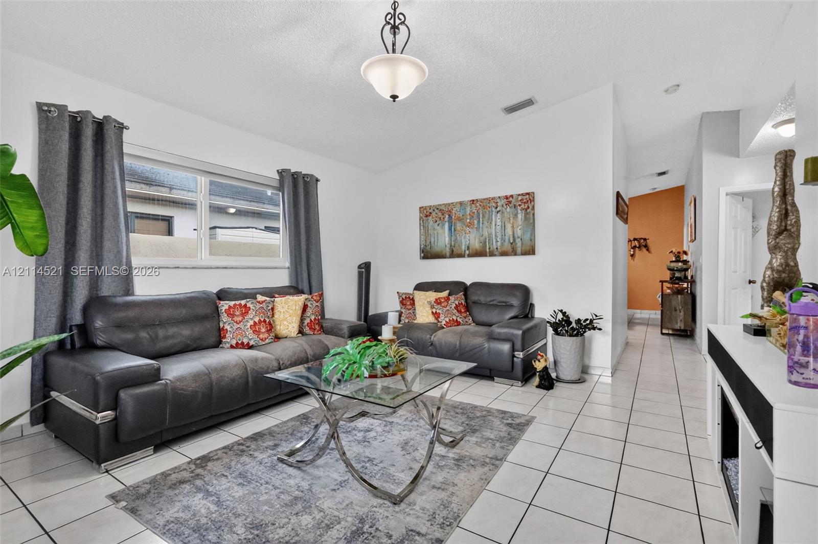 Living area featuring light-colored floor tiling, a single-hung window, and a central pendant light fixture Living area featuring light-colored floor tiling, a single-hung window, and a central pendant light fixture
