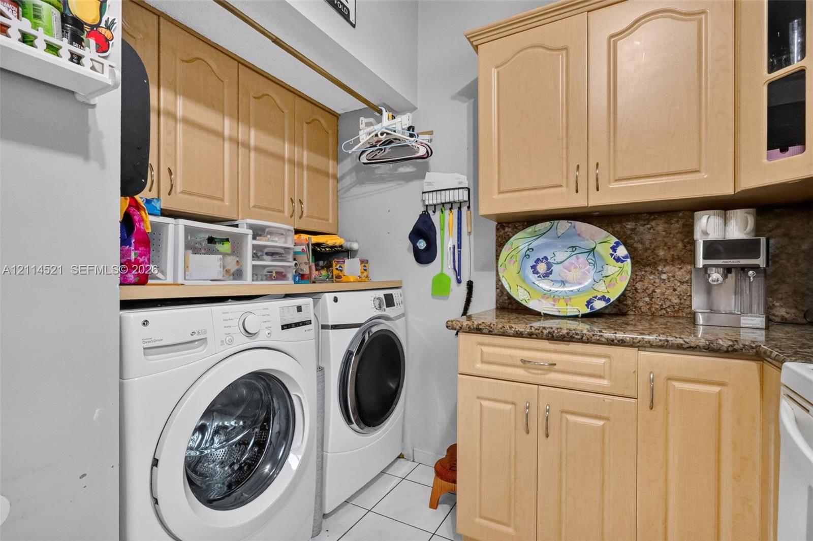 Utility space featuring raised-panel wood cabinetry, natural stone countertops, and tile flooring Utility space featuring raised-panel wood cabinetry, natural stone countertops, and tile flooring