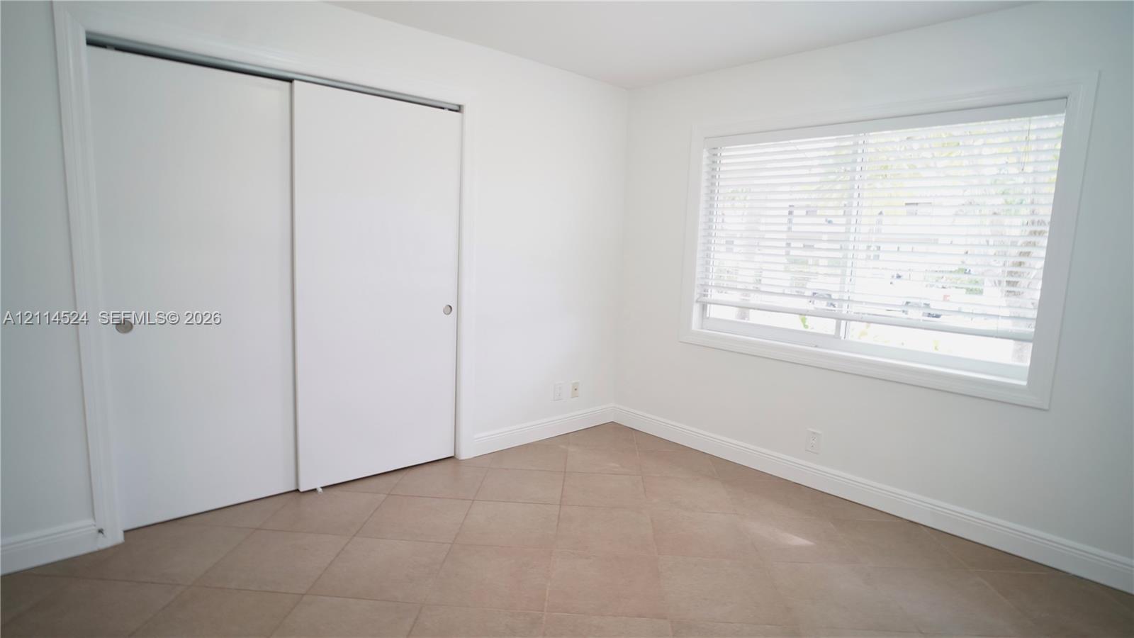 Neutral-toned tile flooring, white sliding closet doors, and a window with horizontal blinds
