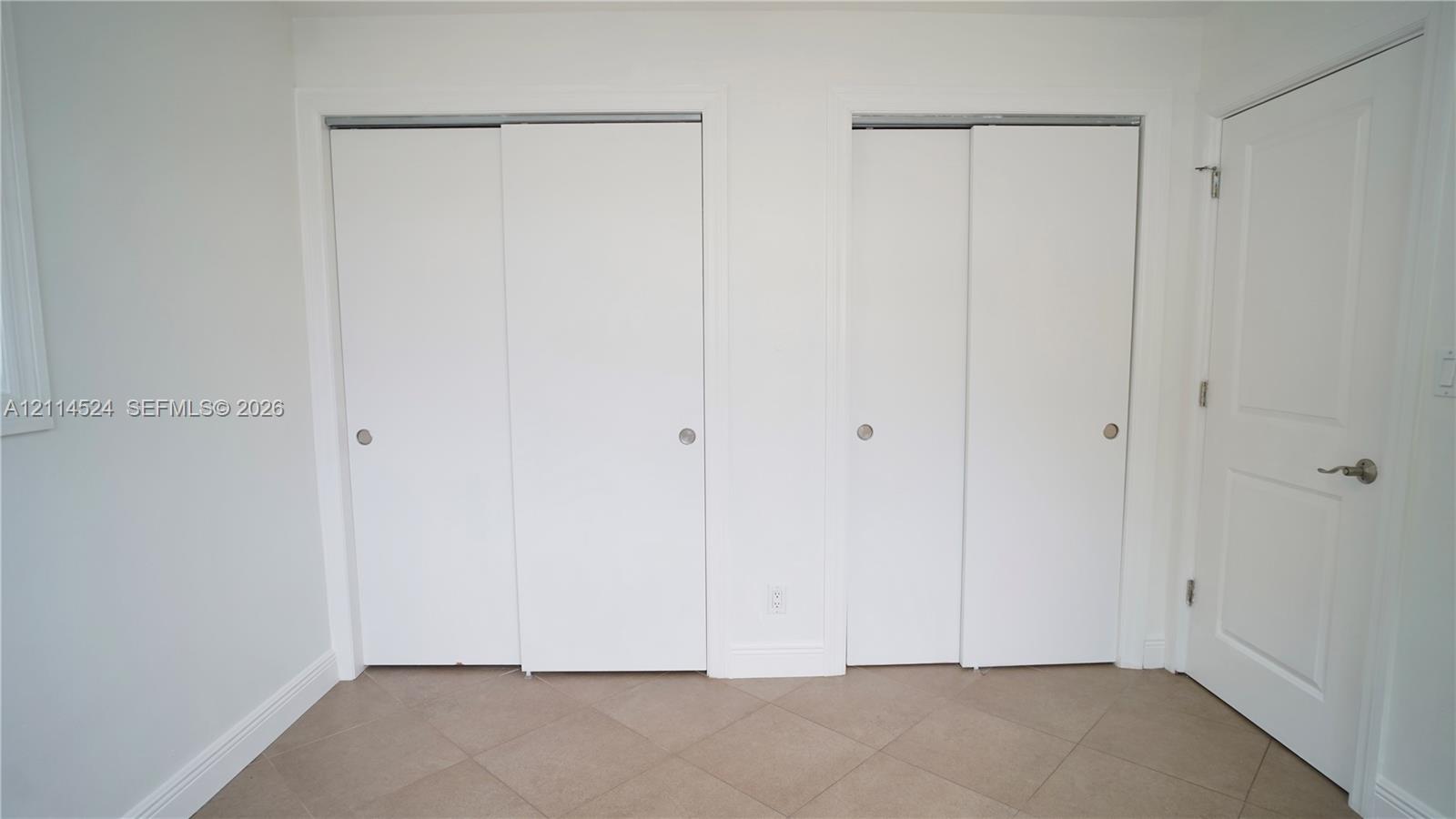 Dual floor-to-ceiling closets with sliding doors, neutral ceramic tile flooring, and a solid-core interior swing door