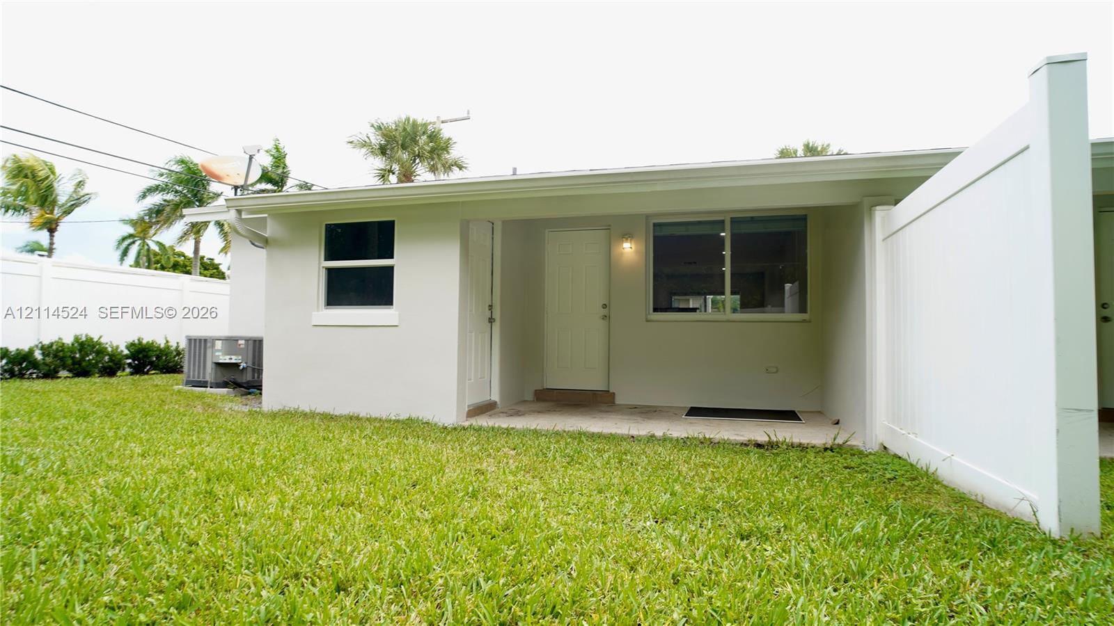 Stucco exterior featuring a covered patio, white privacy fencing, and a manicured lawn