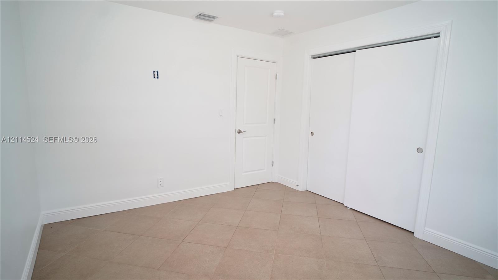 Neutral-toned tile flooring, solid-core interior door, and dual sliding-door closet with clean white finishes