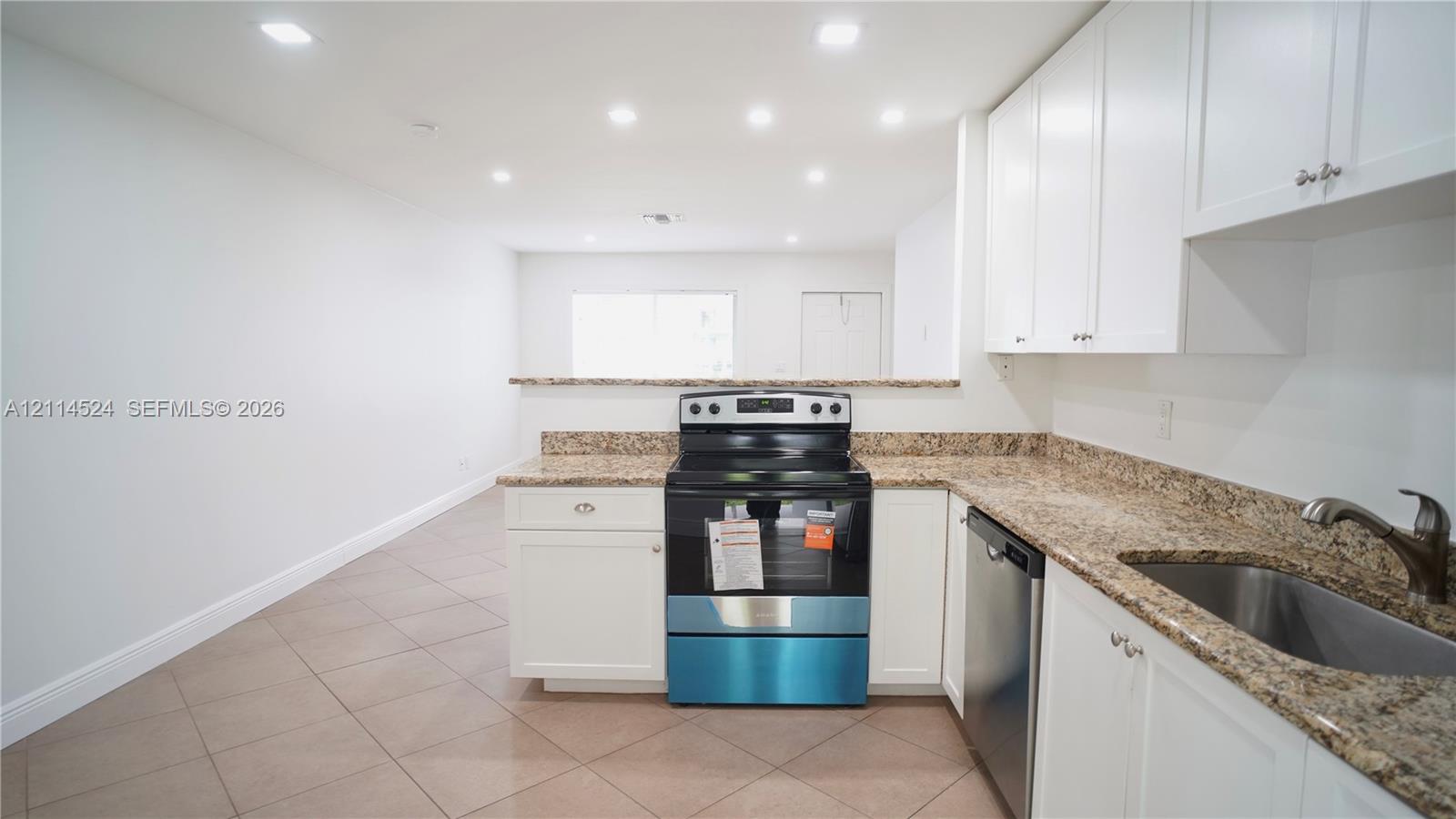 Kitchen featuring white shaker-style cabinetry, stone-patterned countertops, a stainless steel freestanding range, a stainless steel dishwasher, and tiled flooring