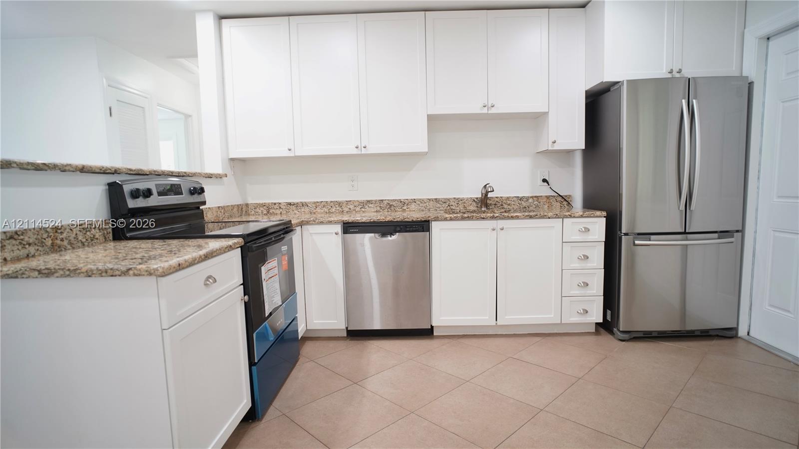 Kitchen featuring white shaker-style cabinetry, stone-patterned countertops, a stainless steel dishwasher, a stainless steel refrigerator, and tiled flooring