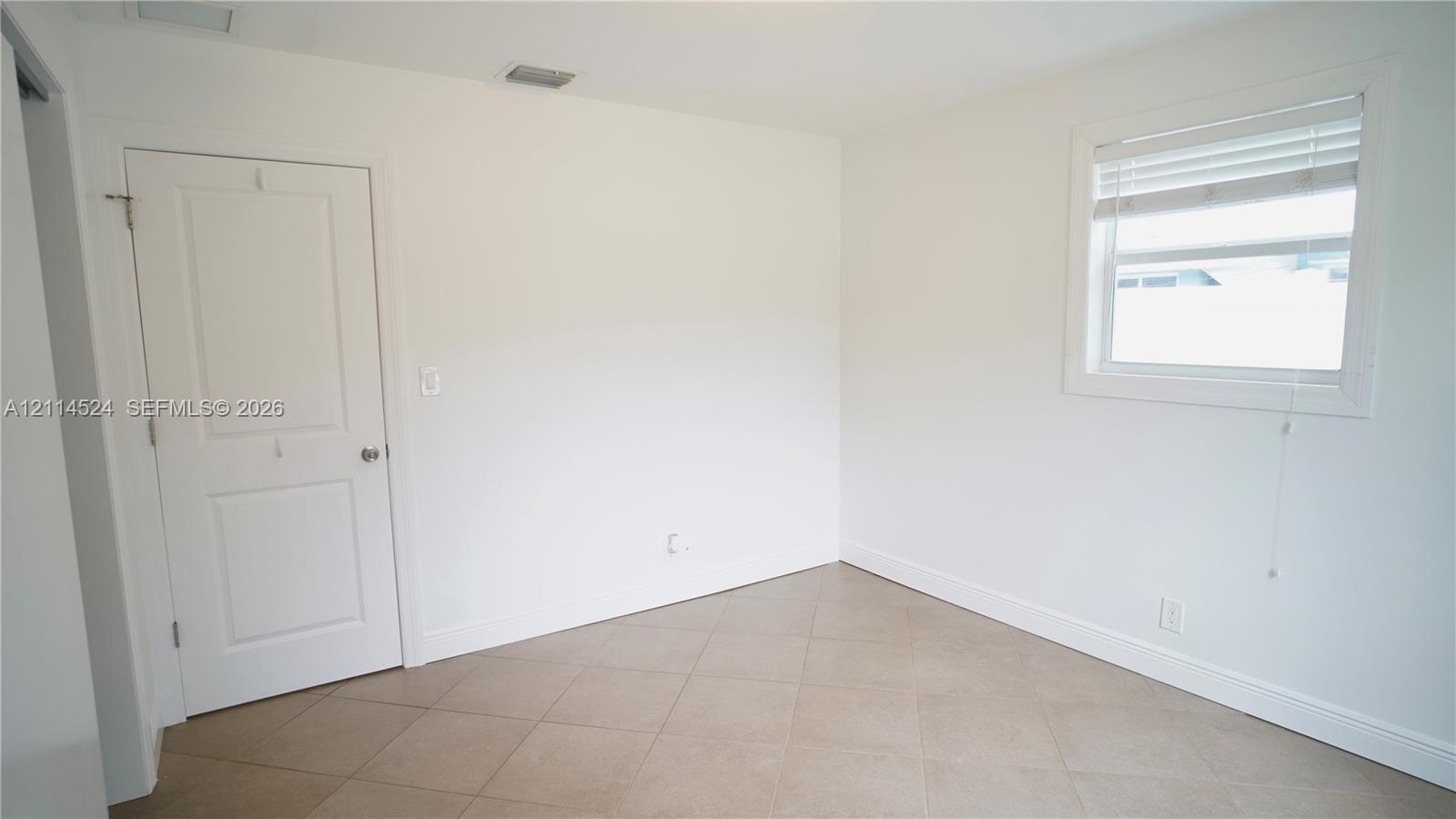 Neutral room interior featuring large-format ceramic tile flooring, a two-panel interior door with brushed metal hardware, and a single-hung window with fitted blinds