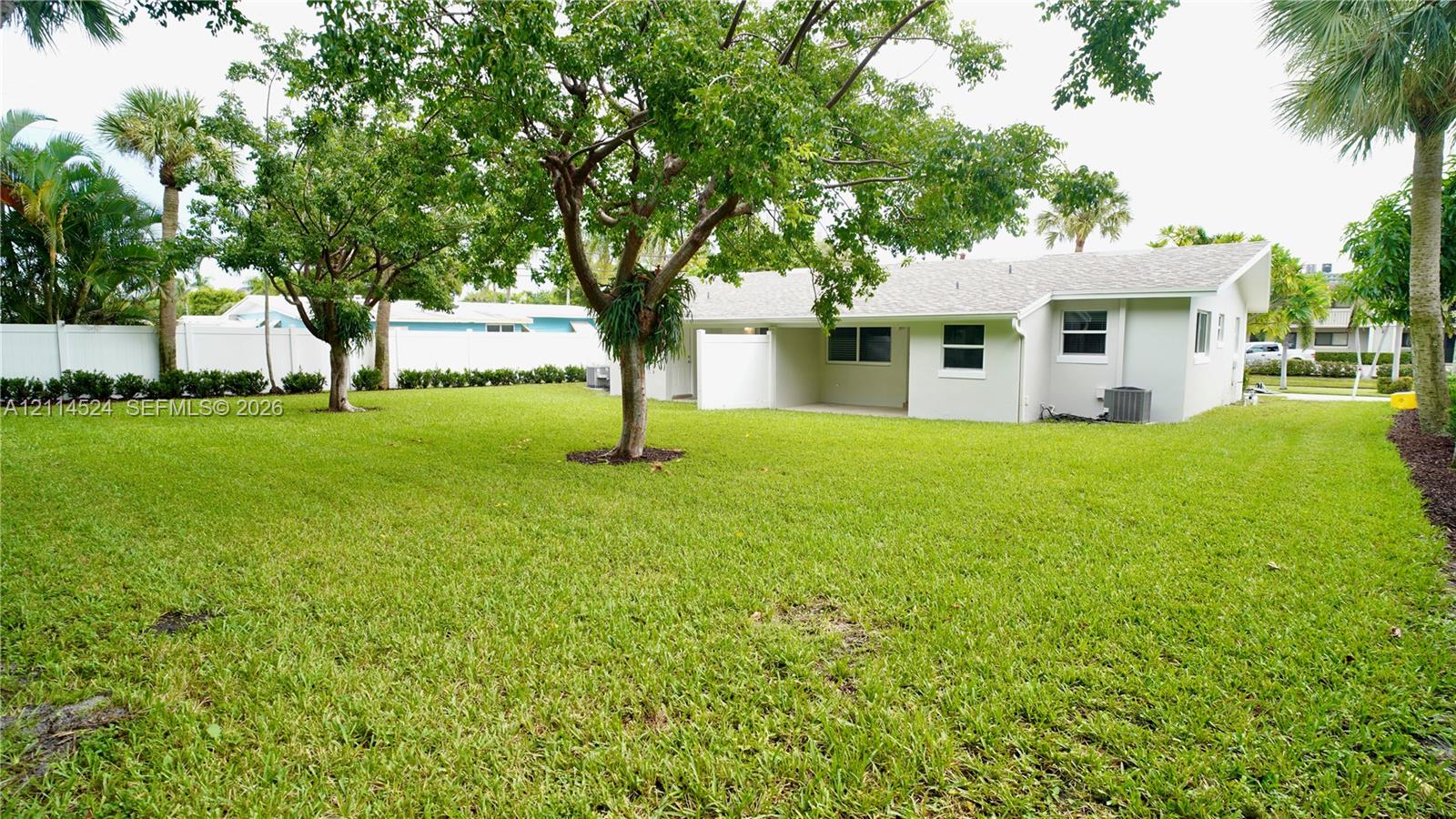 Expansive backyard featuring a sprawling grass lawn, mature shade trees, perimeter privacy fencing, and a concrete patio