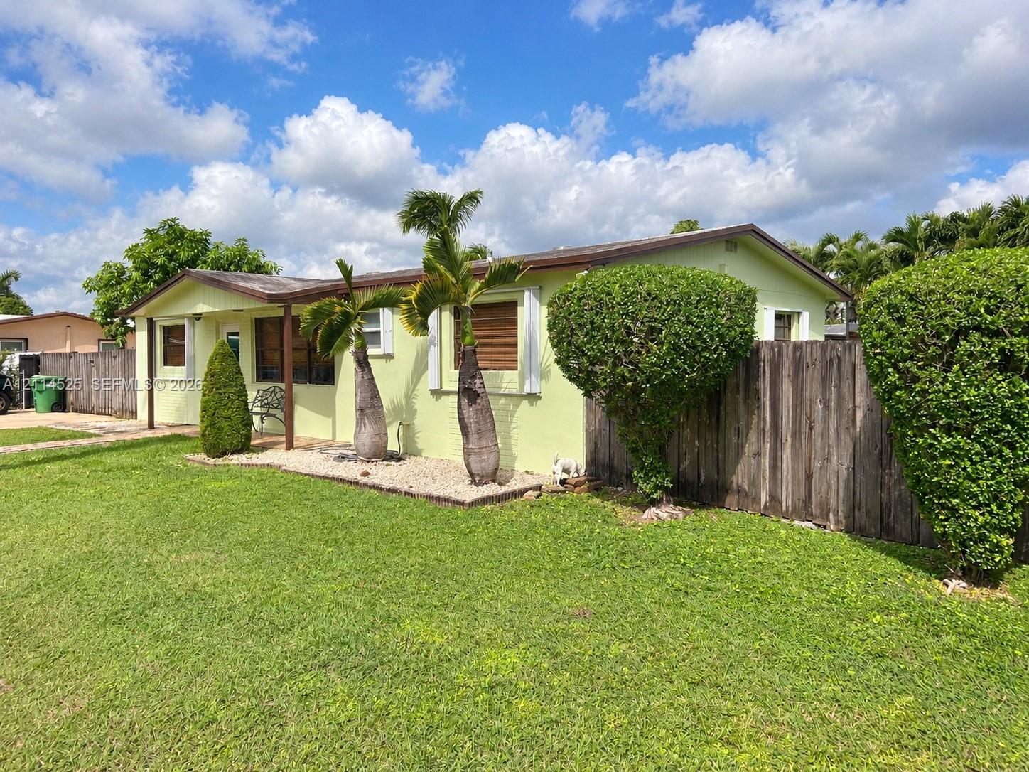 Single-story residence featuring light-toned exterior finish, low-slope roof, covered front entrance, wood-panel fencing, and mature landscaping Single-story residence featuring light-toned exterior finish, low-slope roof, covered front entrance, wood-panel fencing, and mature landscaping