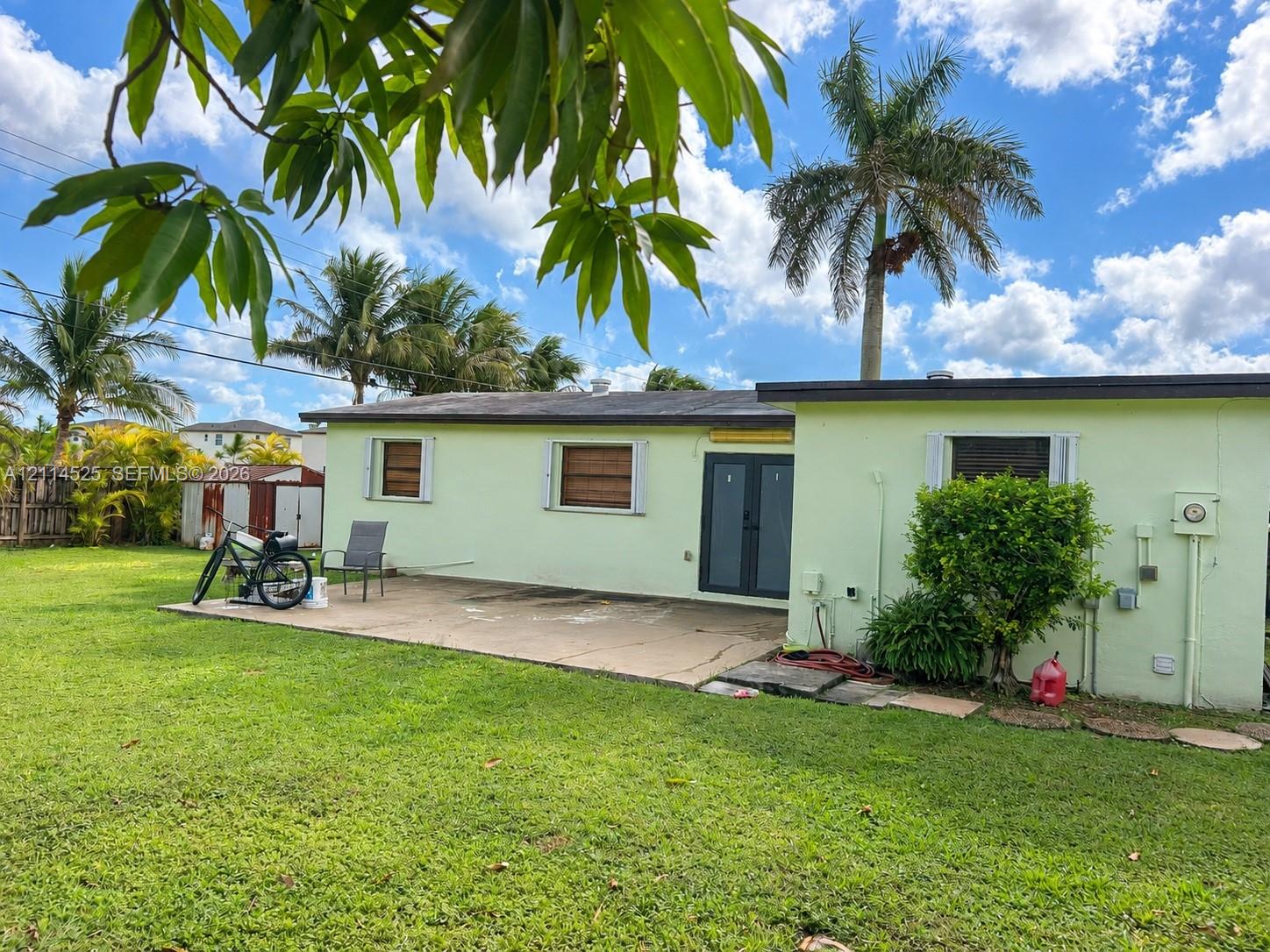Rear exterior featuring a concrete patio, double entry doors, and an expansive lawn with mature palm trees