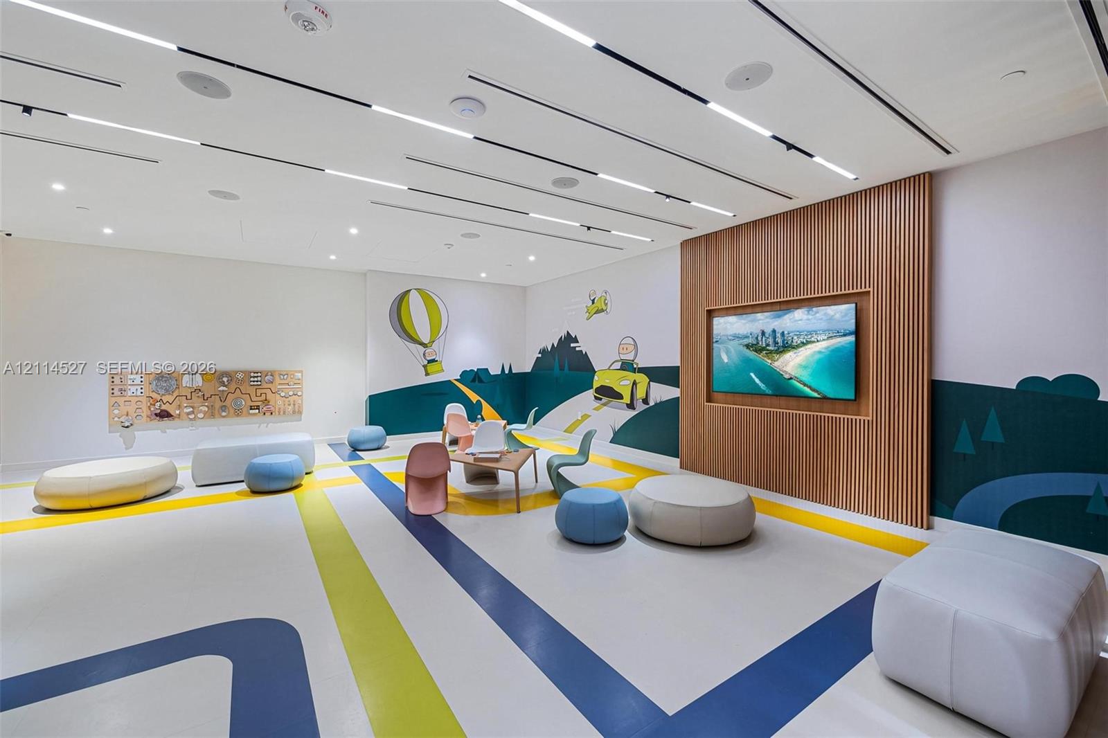 Open-concept room featuring a linear recessed lighting system, integrated ceiling speakers, and a wood-slat accent wall with a wall-mounted display
