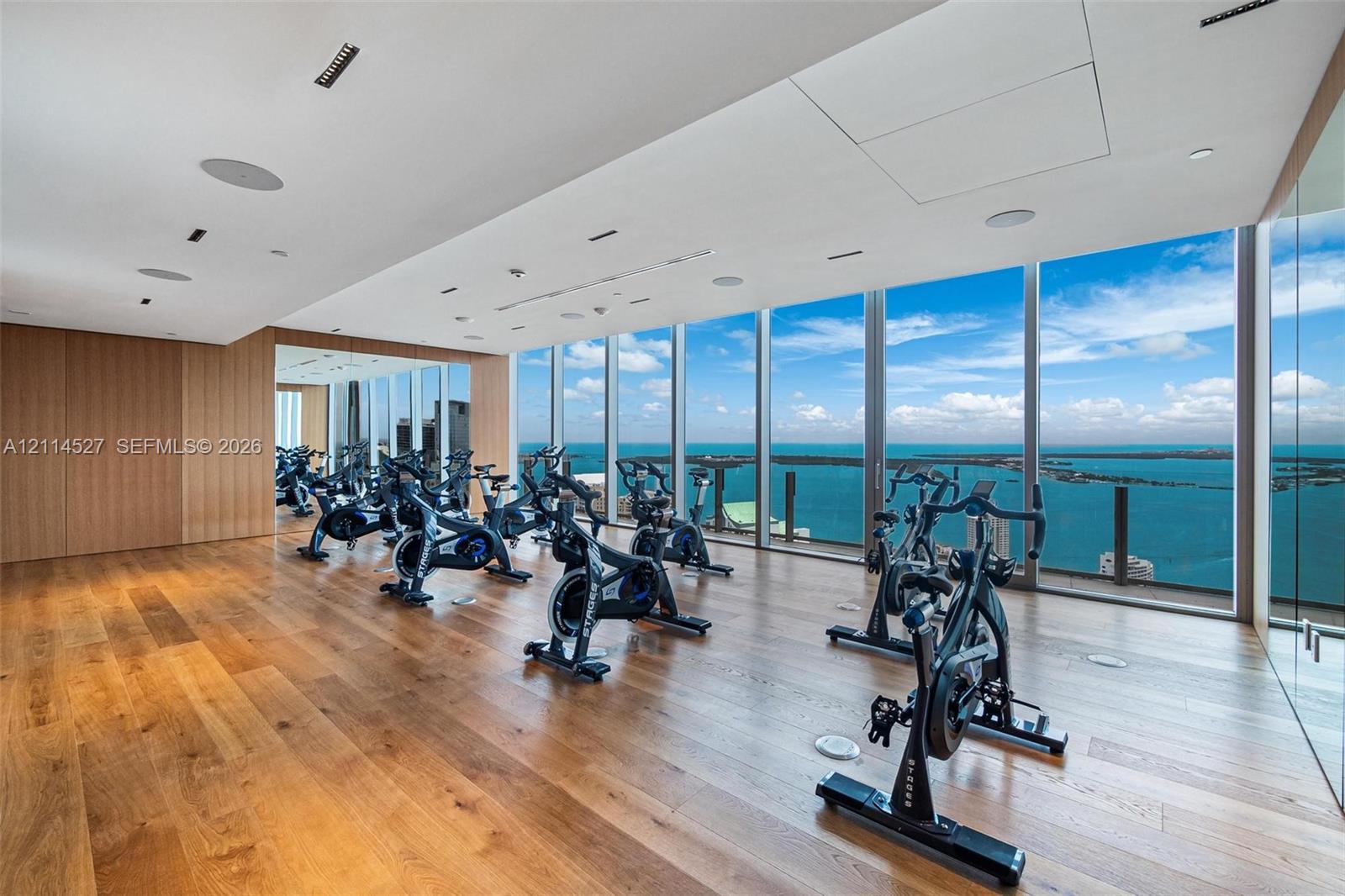 Floor-to-ceiling windows, wood-finish flooring, full-wall mirrored paneling, recessed lighting, and water backdrop