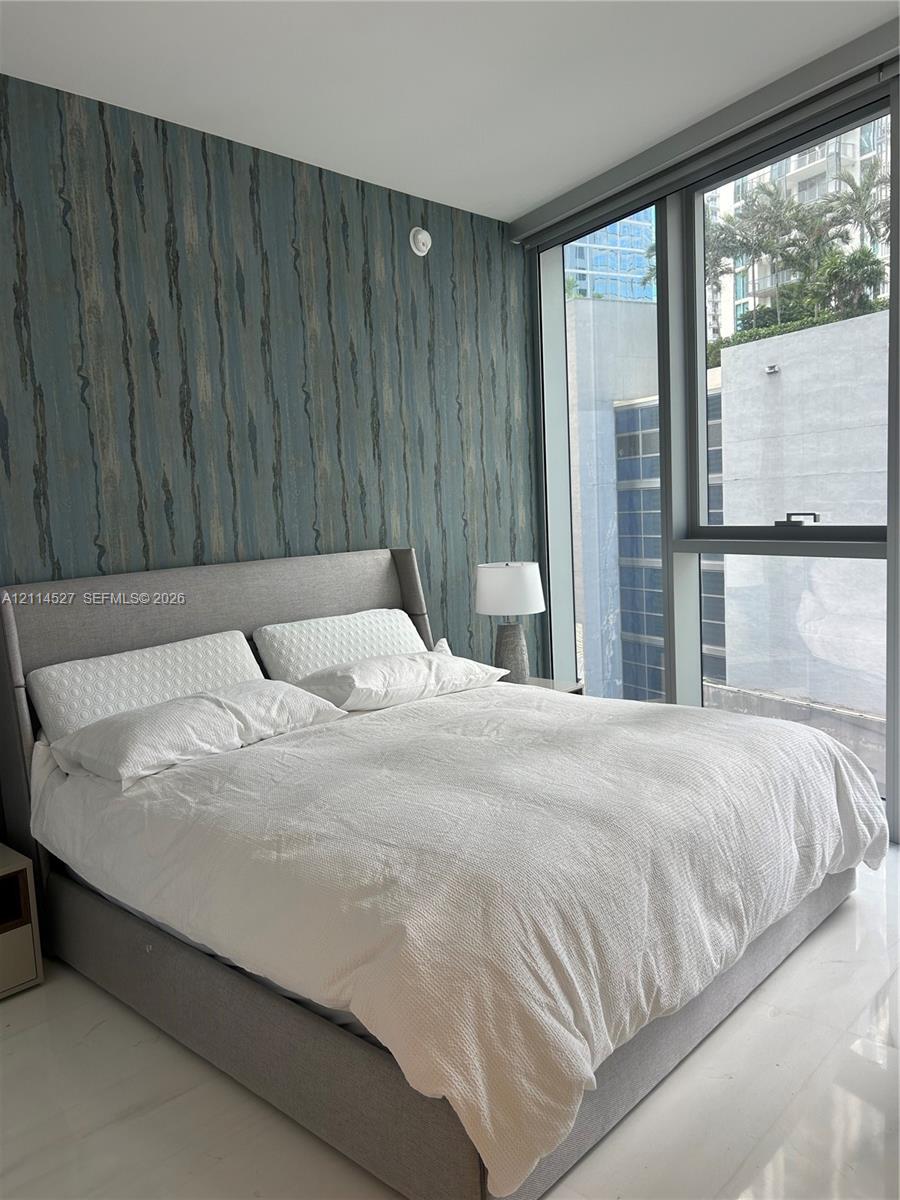 Floor-to-ceiling windows, textured accent wall, and polished tile flooring